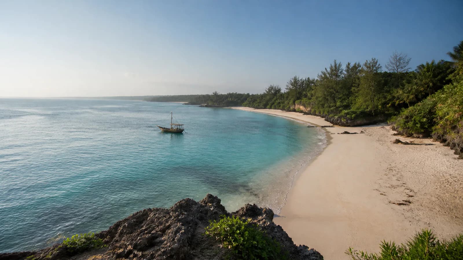 Baia di sabbia chiara sulla costa dell'Africa orientale con un dhow al largo